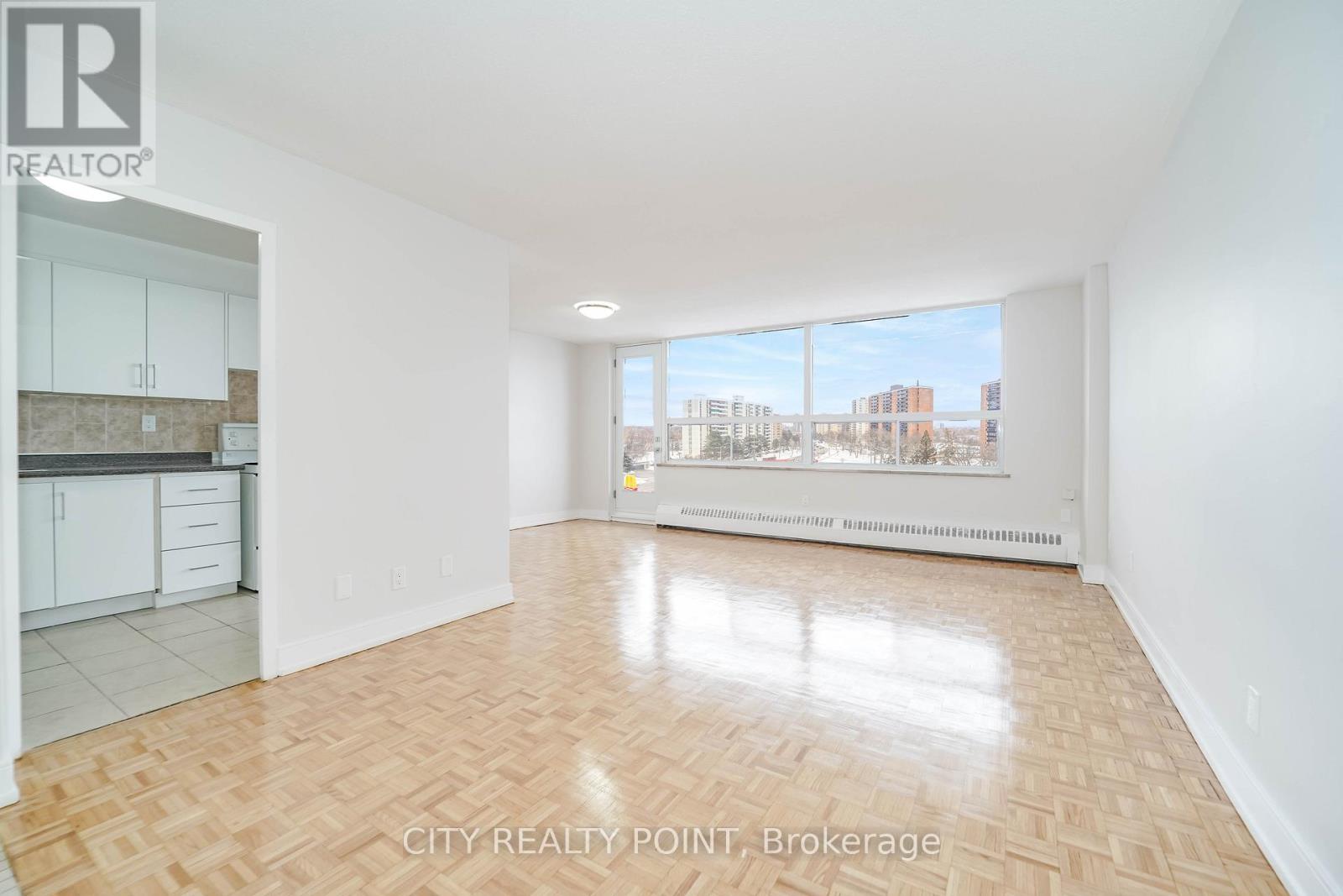 A spacious room with wooden flooring and a view of the city through the window.
