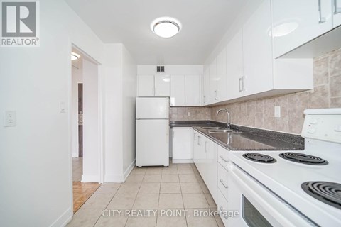 A white refrigerator in a kitchen with white cabinets.