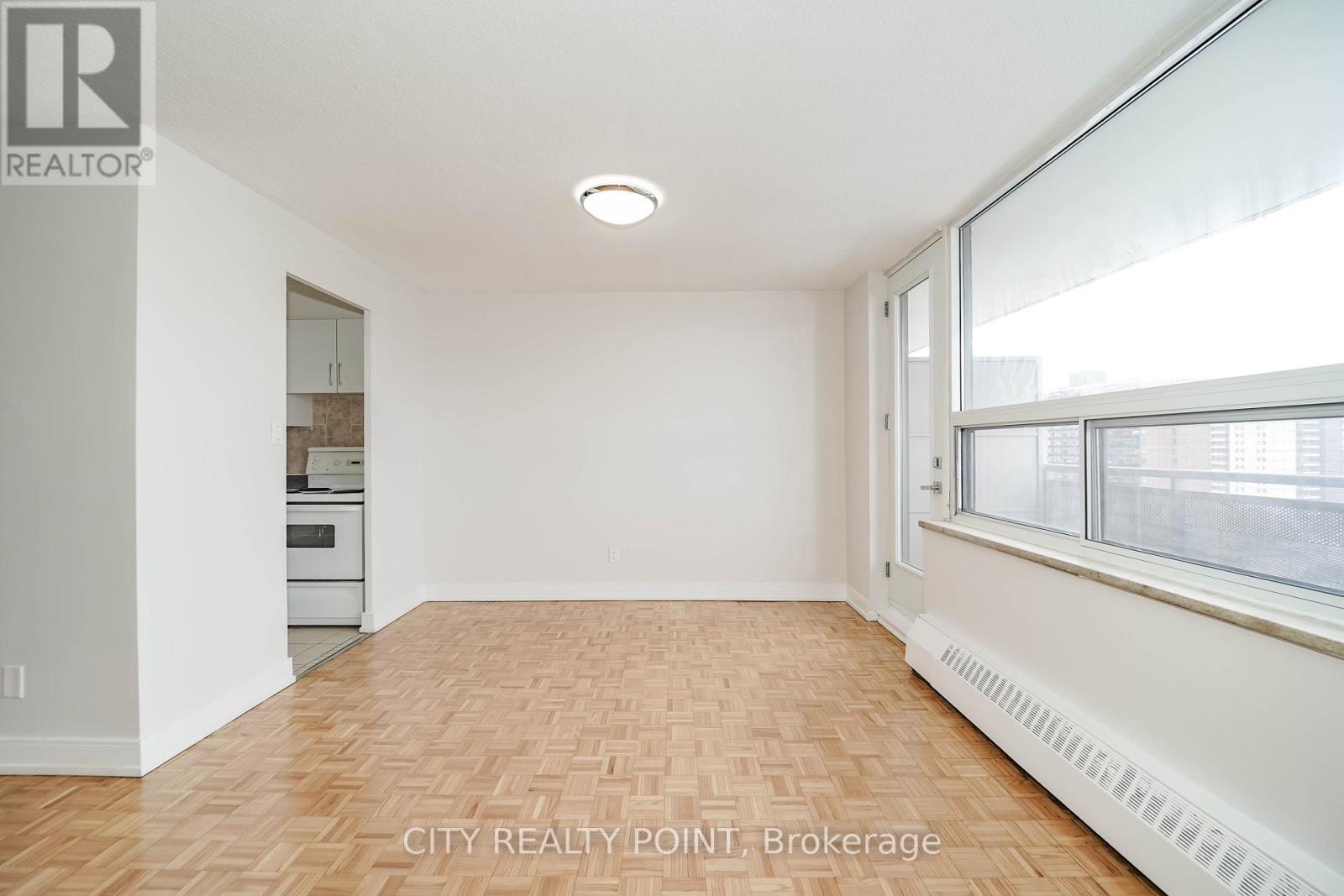 A room with wooden flooring and a window with a view of buildings outside.