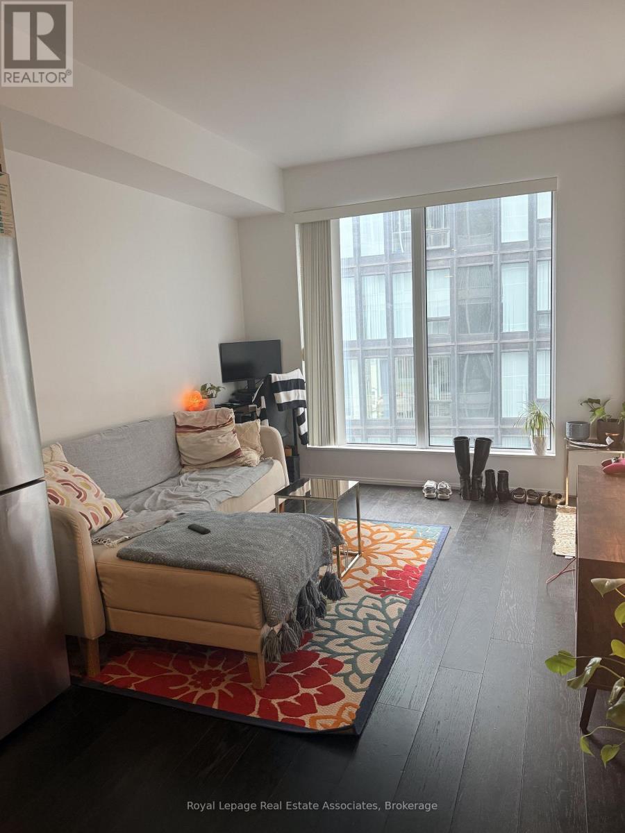 A bedroom with a bed, a couch, a TV, and a window with a view of a building.