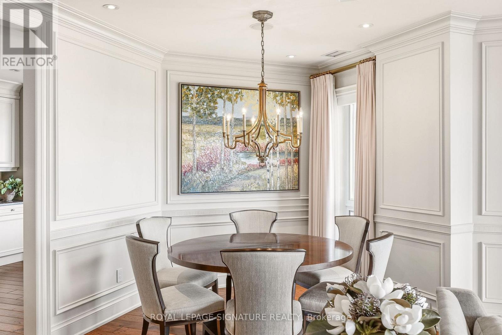 A dining room with a chandelier, a table with chairs, and a painting on the wall.