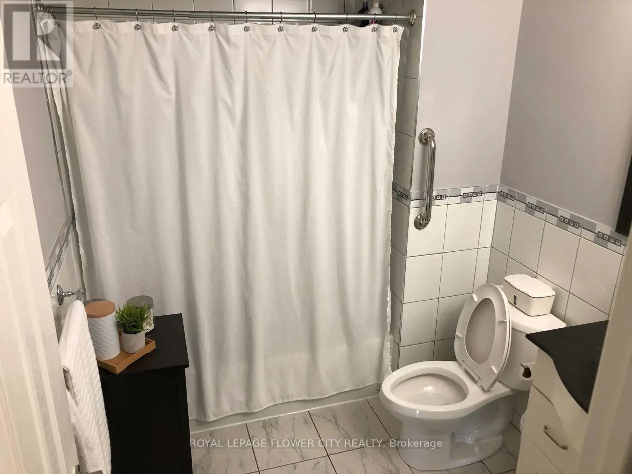 A white shower curtain in a bathroom with a toilet and a small plant on a shelf.