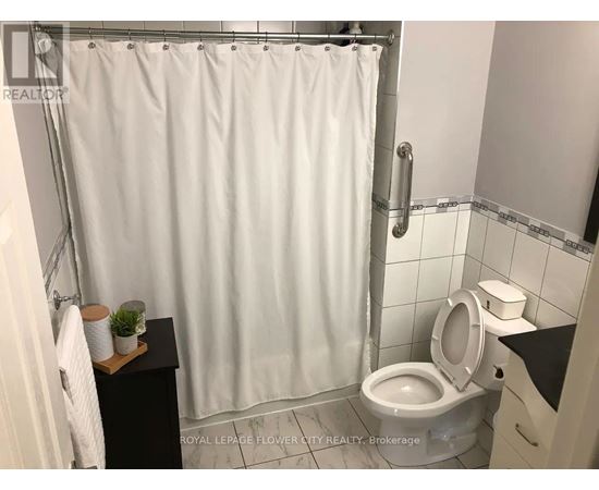 A white shower curtain in a bathroom with a toilet and a small plant on a shelf.