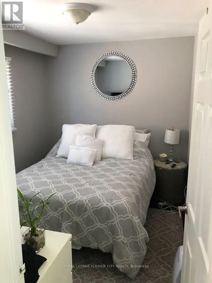 A bedroom with a bed, nightstand, lamp, and a mirror on the wall.