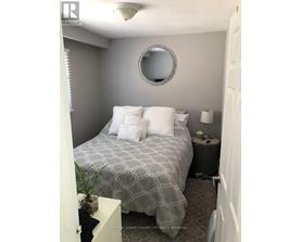 A bedroom with a bed, nightstand, lamp, and a mirror on the wall.
