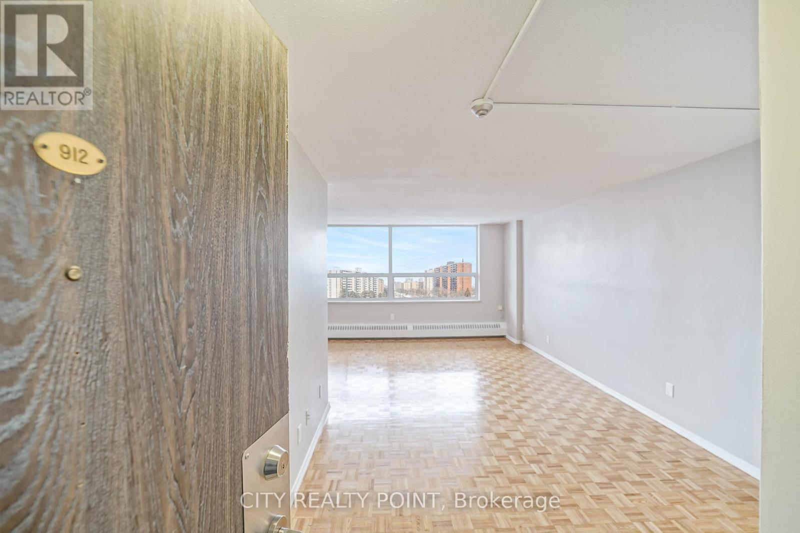 A hallway with a wooden door and a view of a city skyline through the window.