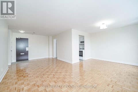 A spacious room with wooden flooring and white walls, featuring a refrigerator and a small kitchenette.