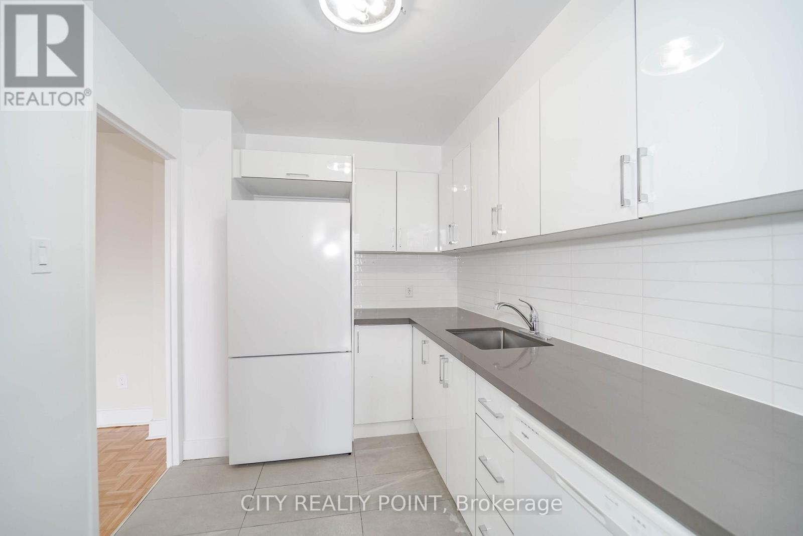 A white refrigerator is in a kitchen with white cabinets.