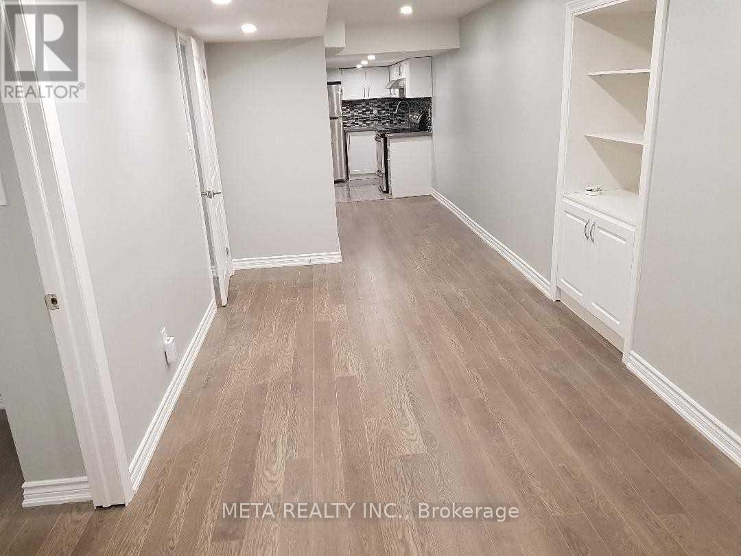 A room with white walls and wooden flooring, with a kitchen area visible in the background.