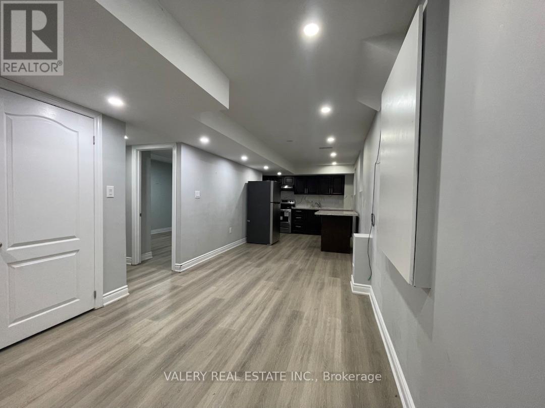 A hallway with wood flooring and white walls, leading to a dark room with a desk.