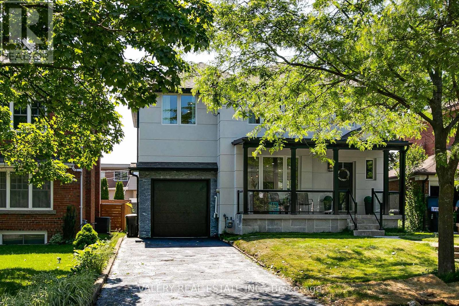A modern house with a driveway and trees in the front yard.