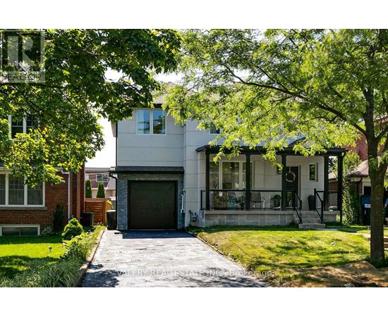 A modern house with a driveway and trees in the front yard.