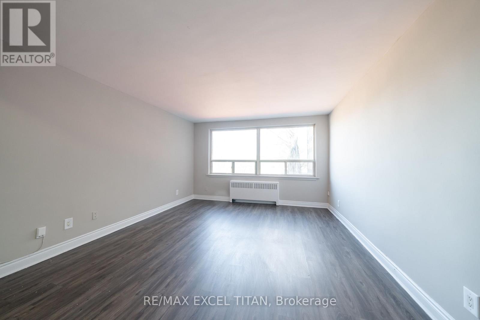 A spacious room with wood flooring and a window with blinds.