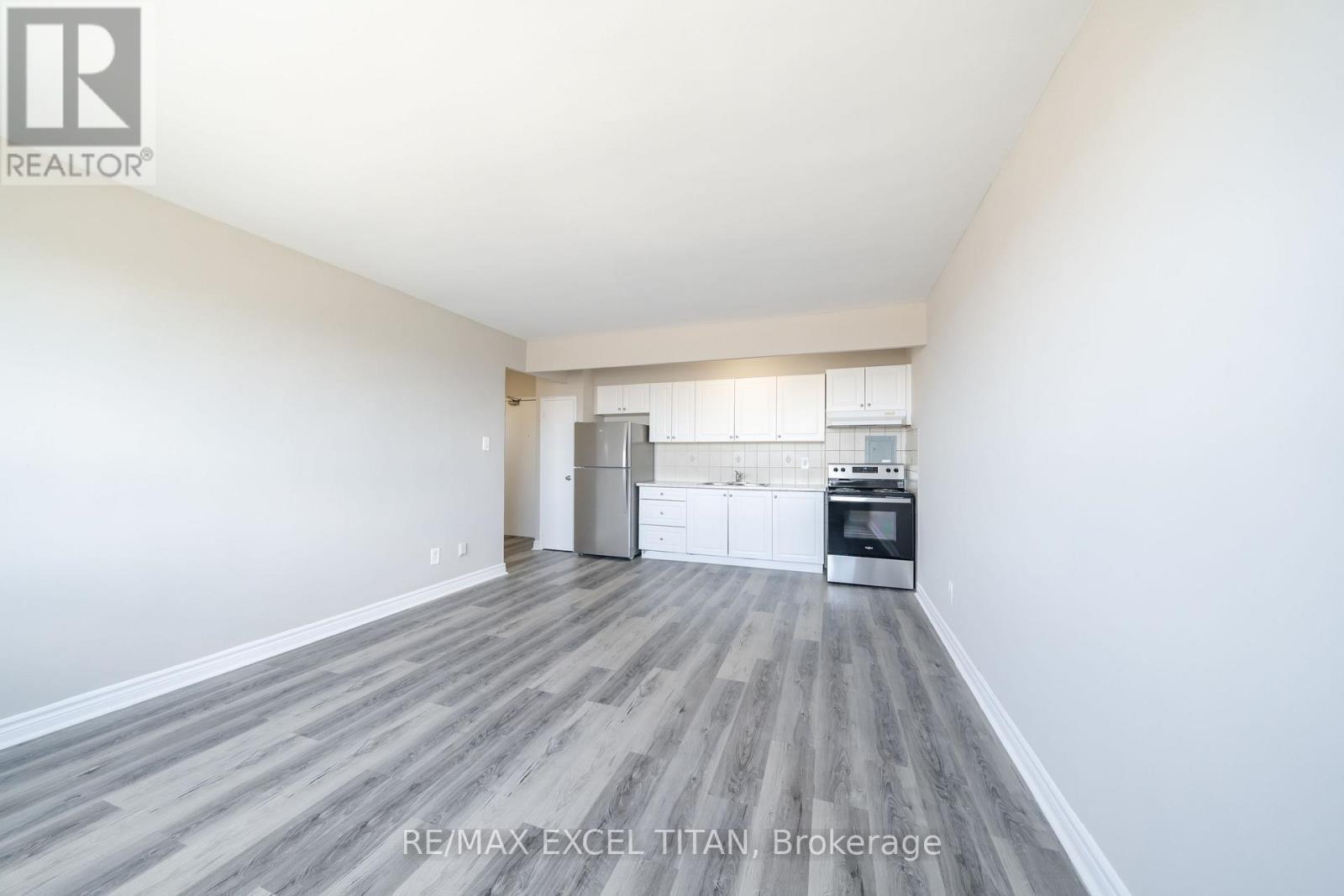 A spacious, empty room with a kitchenette in the background.