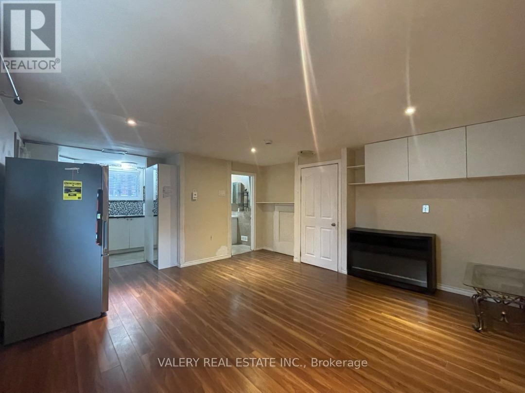 A spacious living room with wood flooring and a black refrigerator.