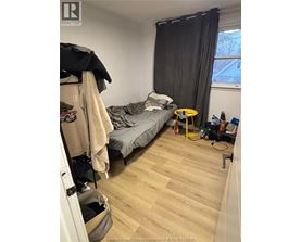 A bedroom with a bed, a chair, and a window with black curtains.
