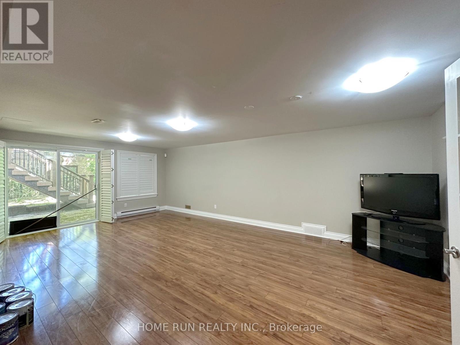 A spacious room with wooden flooring and a television on a stand.