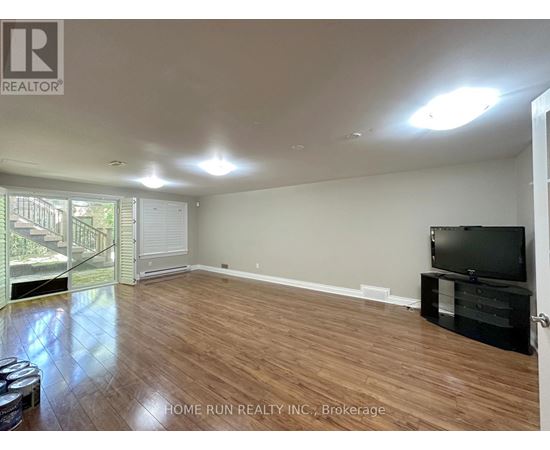 A spacious room with wooden flooring and a television on a stand.