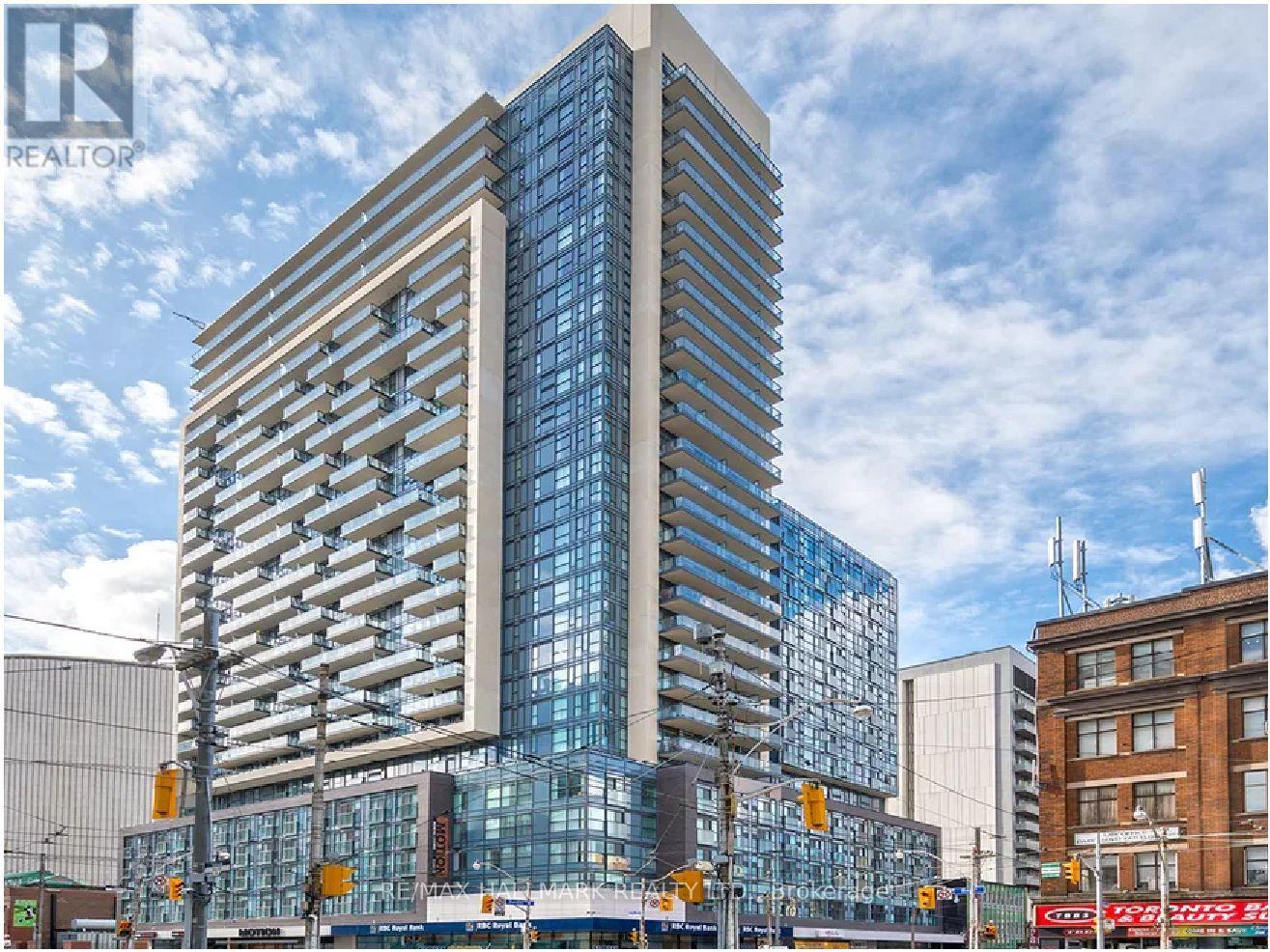 A tall, modern glass building stands in the foreground of a city street.