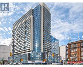 A tall, modern glass building stands in the foreground of a city street.