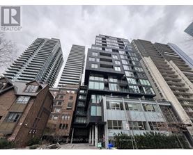 A tall building with a glass facade stands in front of other buildings.