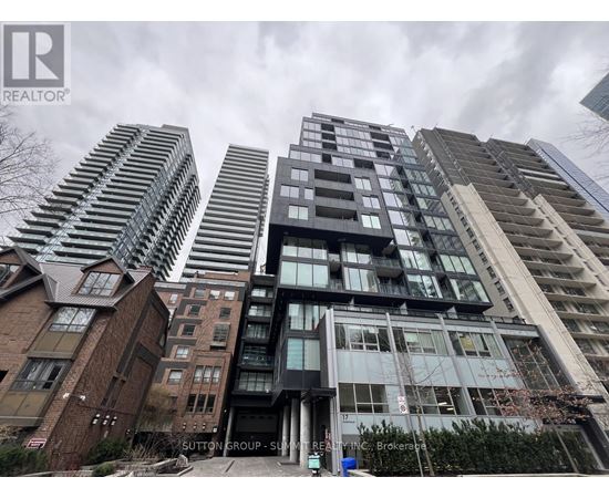 A tall building with a glass facade stands in front of other buildings.