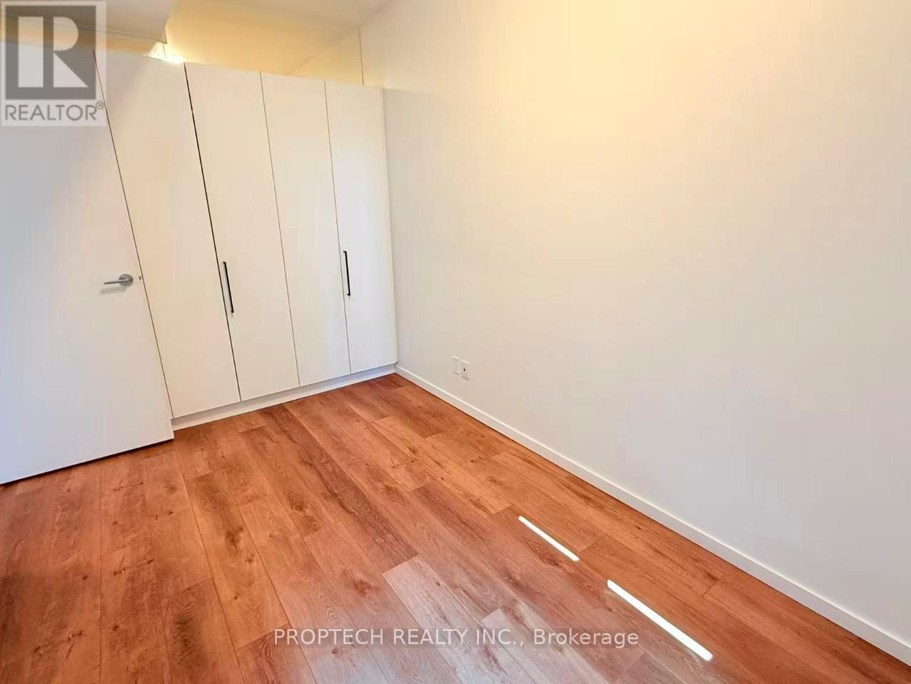 A room with wooden flooring and white walls, featuring a set of white cupboards.