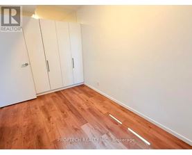 A room with wooden flooring and white walls, featuring a set of white cupboards.