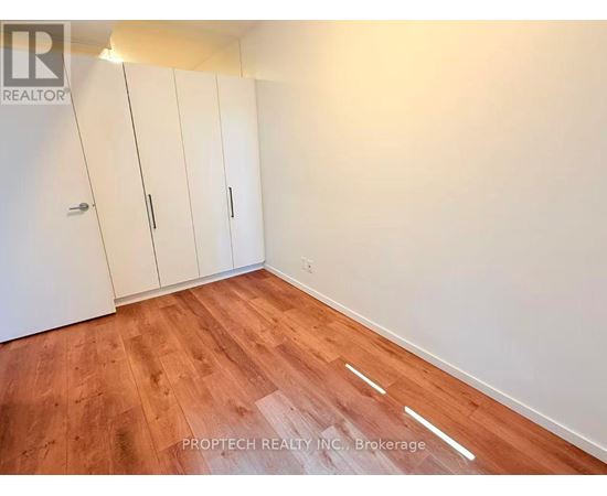A room with wooden flooring and white walls, featuring a set of white cupboards.