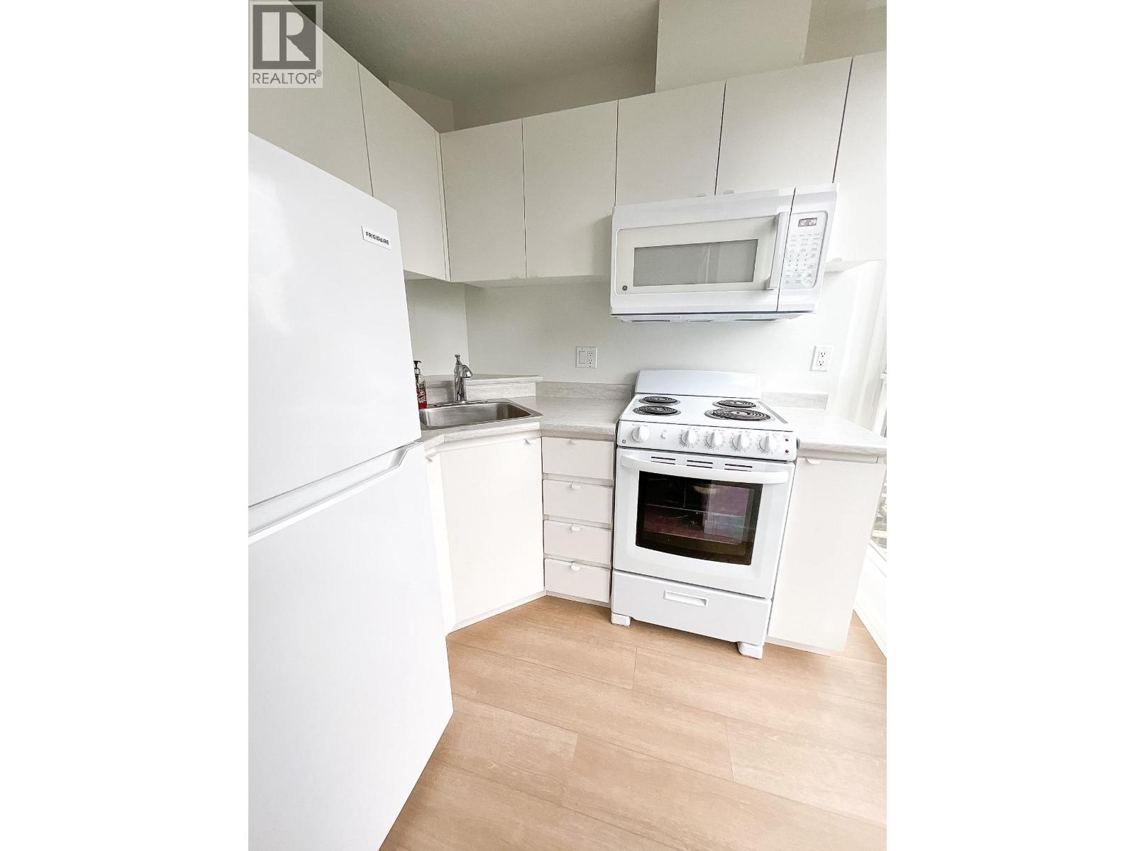 A white kitchen with a refrigerator, microwave, and stove.