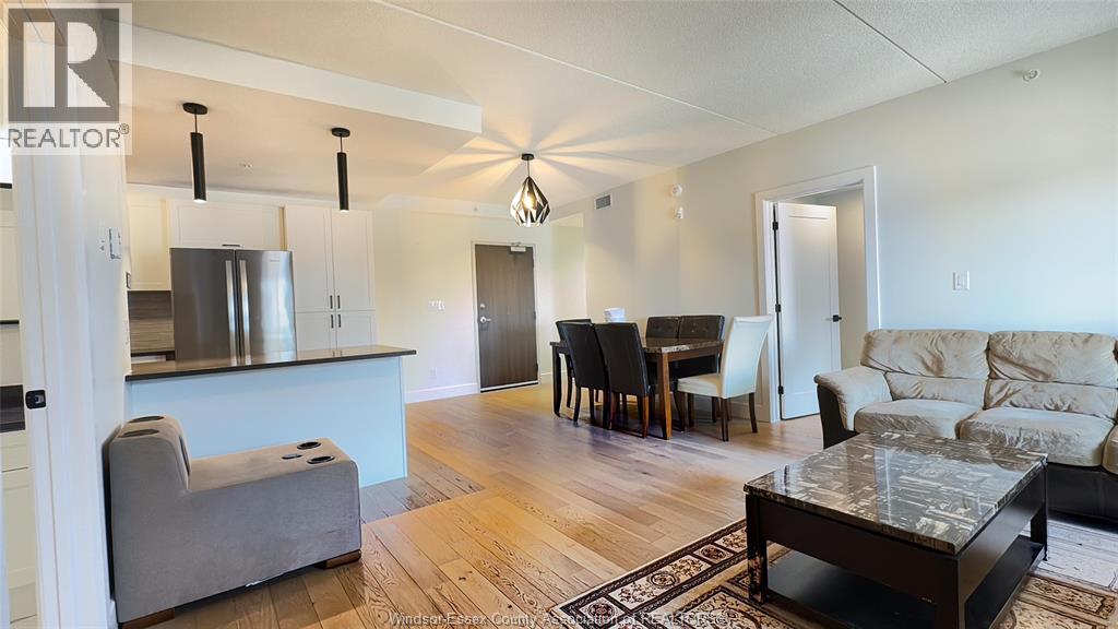 A living room with a grey couch, a dining table with chairs, and a kitchen area with a refrigerator and stove.