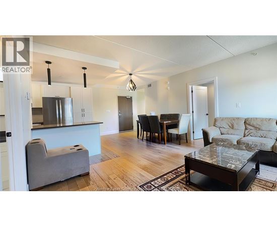A living room with a grey couch, a dining table with chairs, and a kitchen area with a refrigerator and stove.