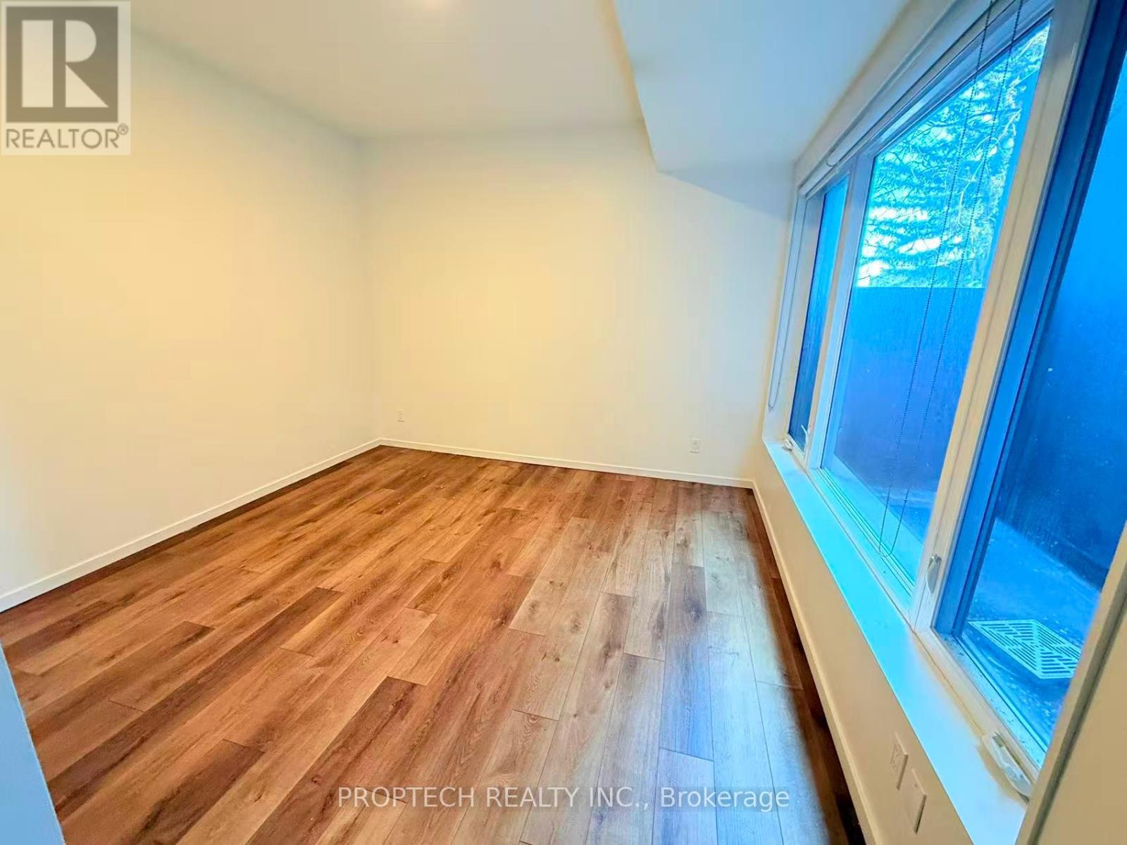 A room with wooden flooring and a window showing trees outside.