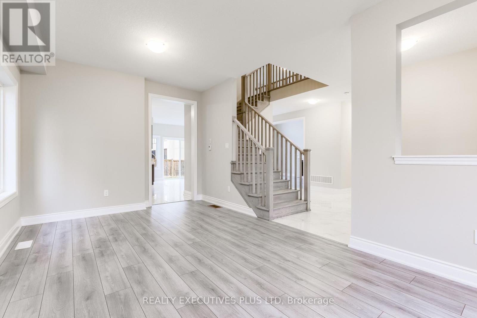 A spacious room with a wooden staircase and grey flooring.