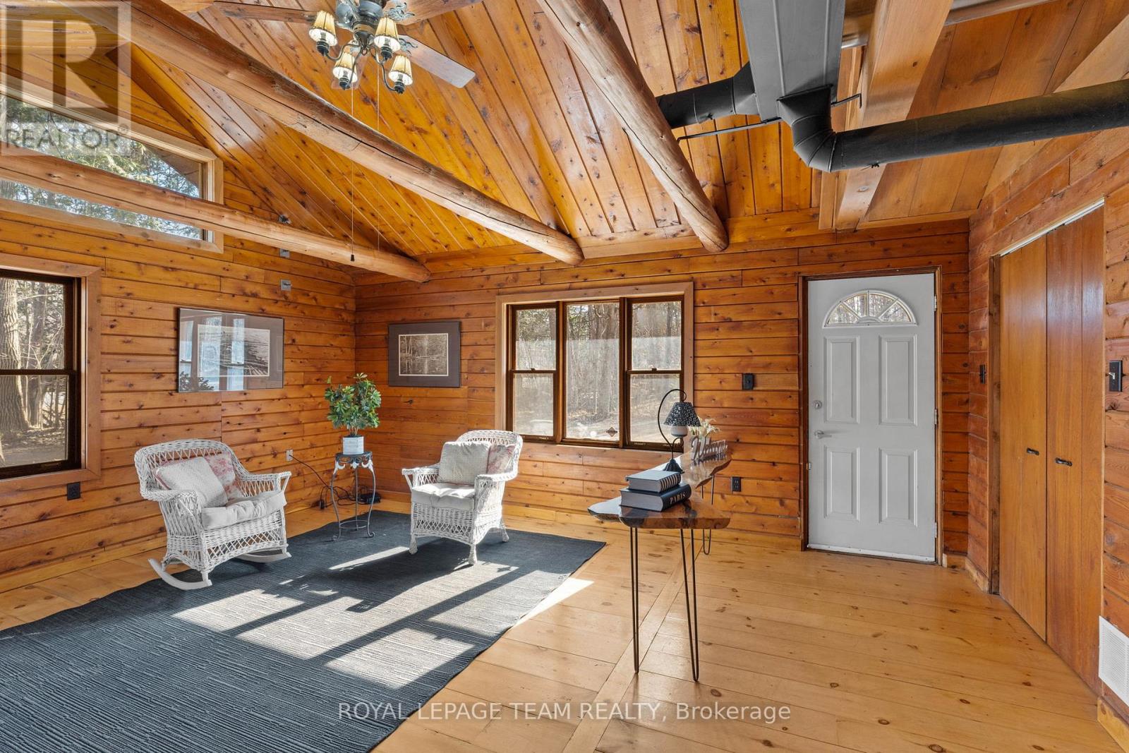A cozy living room with wooden walls and ceiling, furnished with a sofa, armchairs, and a coffee table.