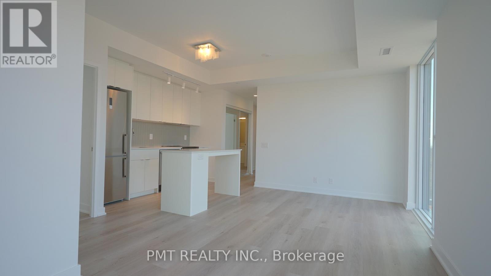 A real estate listing photo of a white interior space with a kitchen area.
