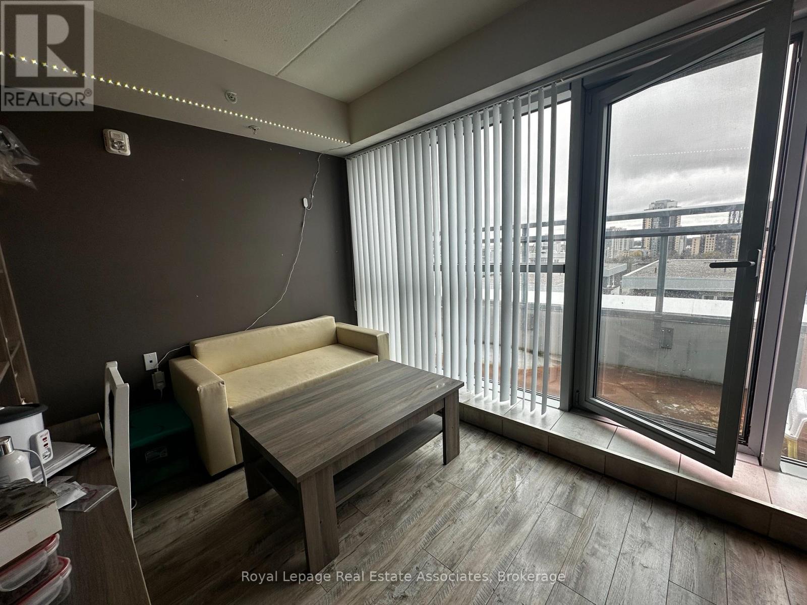 A room with a couch, a table, and a window with blinds.