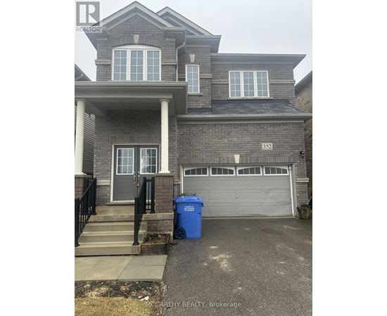 A two-story house with a garage and a blue trash bin in front.