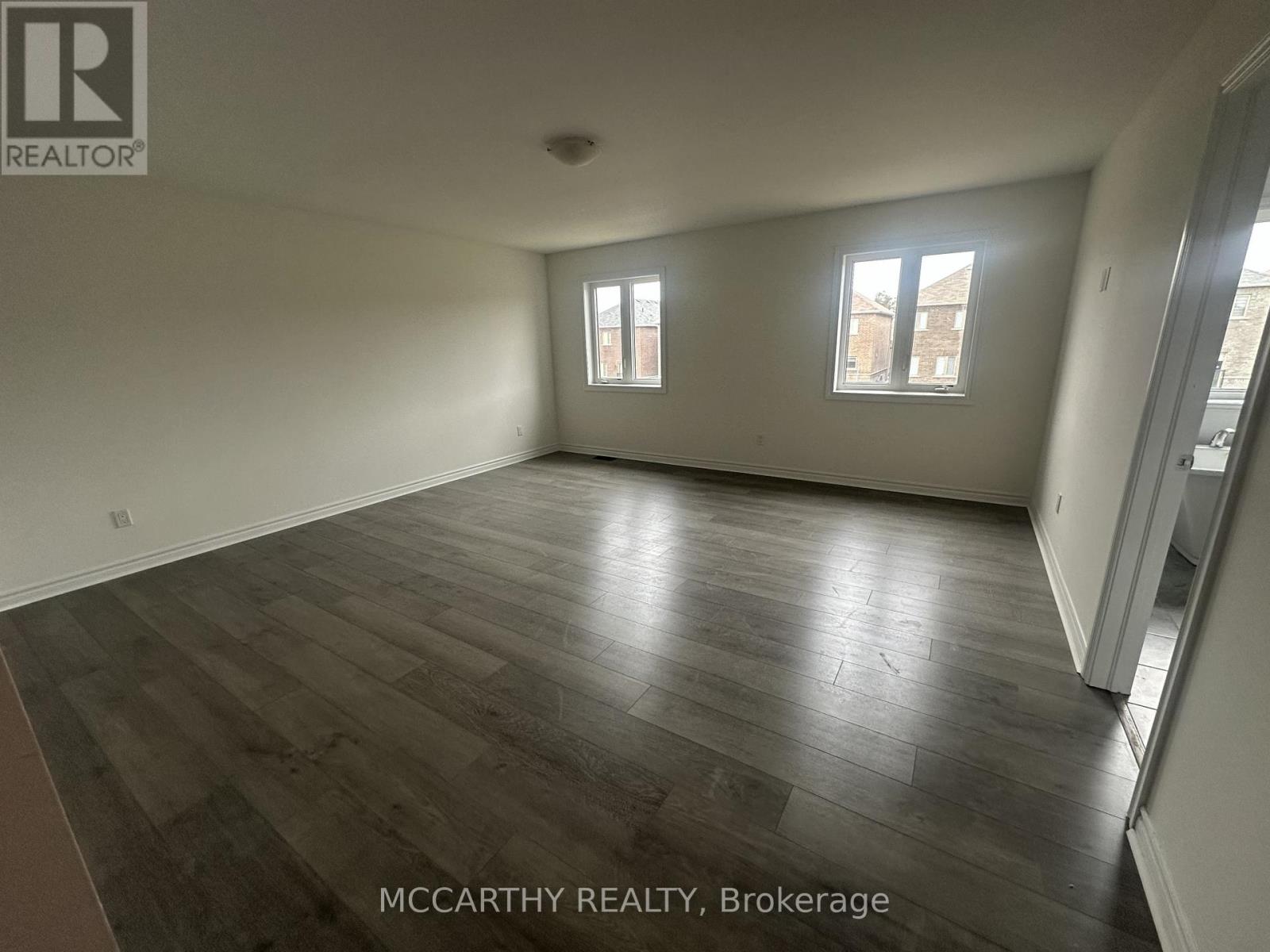 A spacious room with wood flooring and two windows.