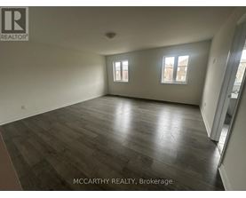 A spacious room with wood flooring and two windows.