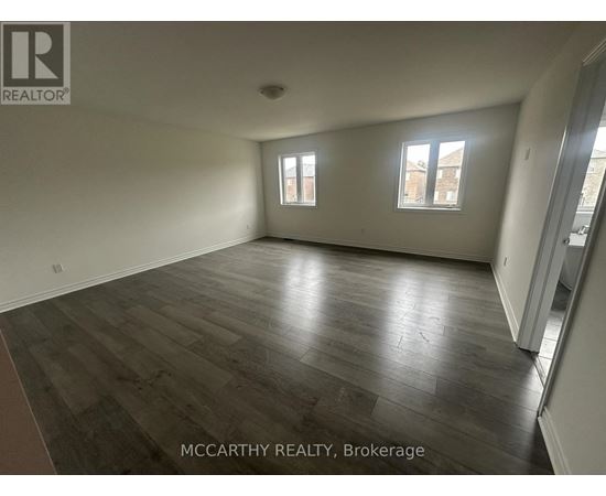 A spacious room with wood flooring and two windows.