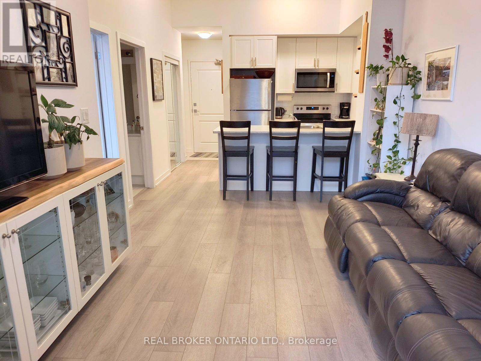 A living room with a black leather couch and a kitchen area in the background.