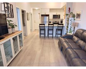 A living room with a black leather couch and a kitchen area in the background.