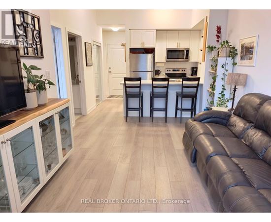 A living room with a black leather couch and a kitchen area in the background.