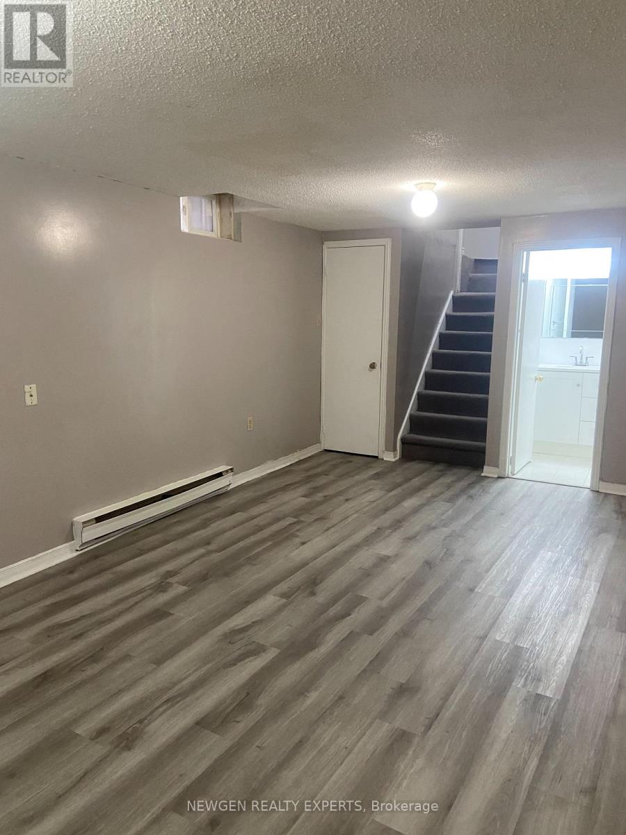 A room with wooden flooring and a staircase leading to another room.