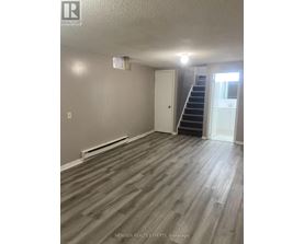 A room with wooden flooring and a staircase leading to another room.