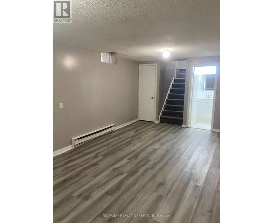 A room with wooden flooring and a staircase leading to another room.