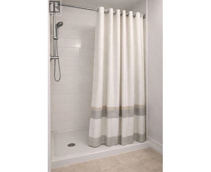 A white shower curtain with grey stripes hangs in a white tiled shower.