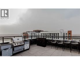 A balcony with barbecue grills and chairs overlooking a cityscape.