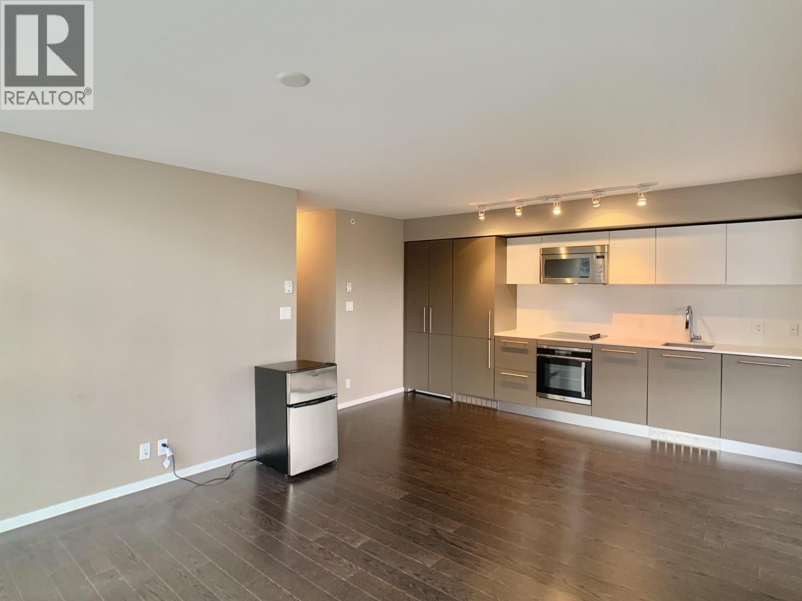 A spacious living room with a kitchen area in the background.